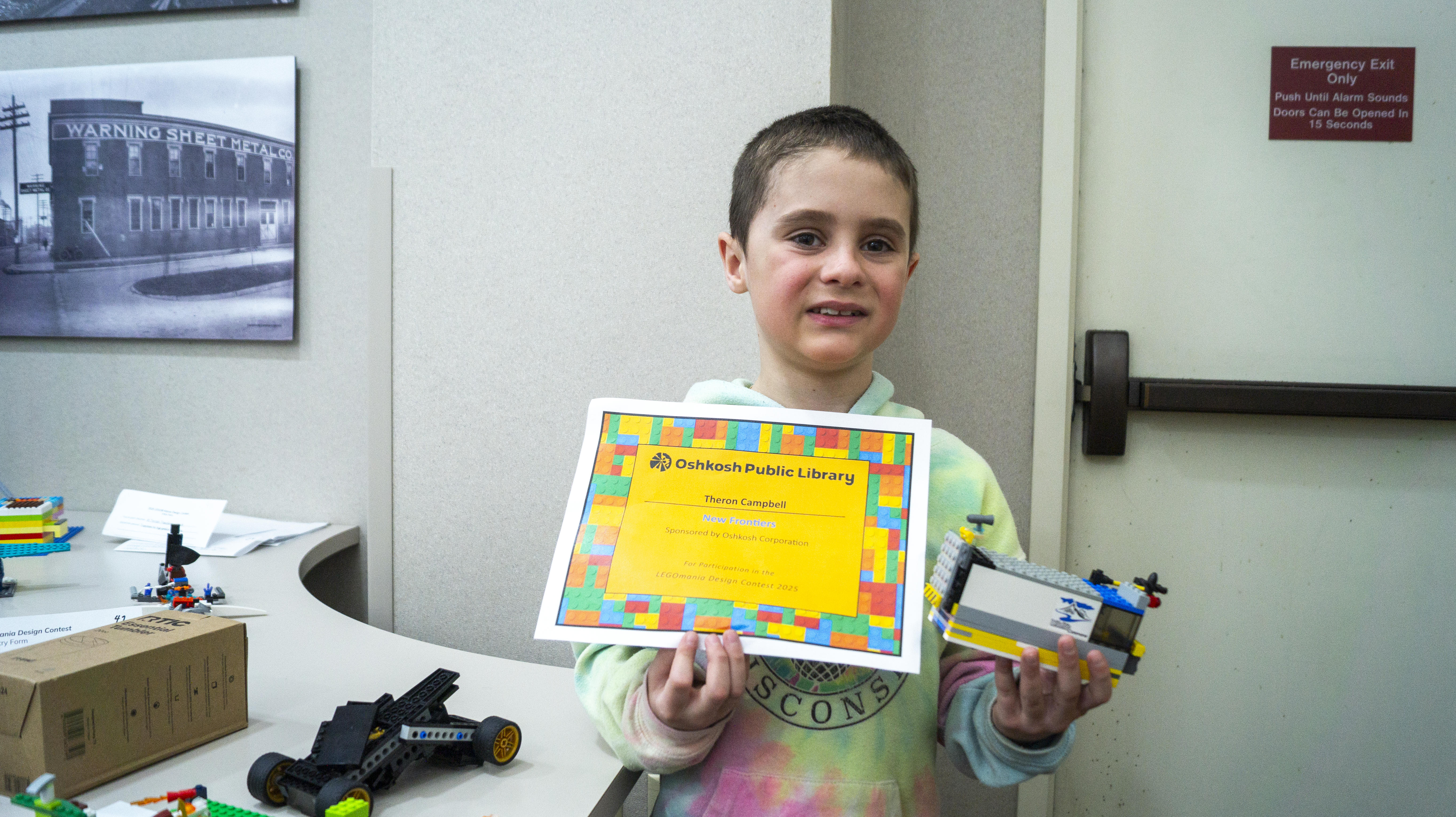 A child holding a certificate and holding his Lego creation.