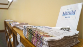 A stack of newspapers from the Oshkosh herald in the foreground. 